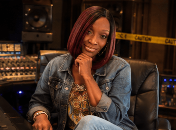 Smiling woman with reddish-brown hair poses in a recording studio wearing a denim jacket.